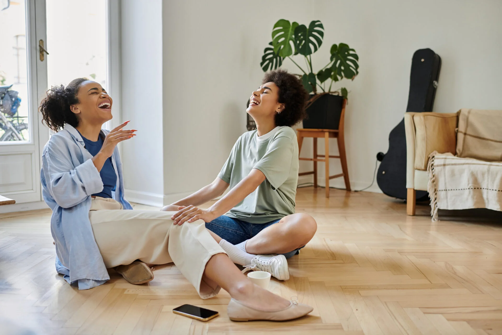 Two friends laughing together on the floor of their new home